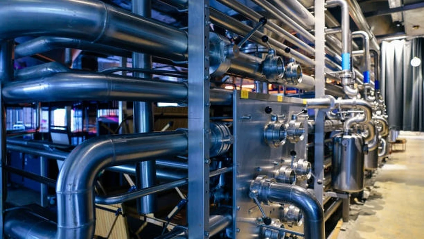 A dense refinery pipe rack in bright midday sun.